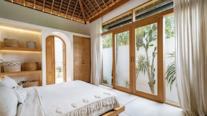 A bedroom with a large bed, wooden ceiling, and sliding glass doors to a garden. - Villa KerangSue (Canggu)