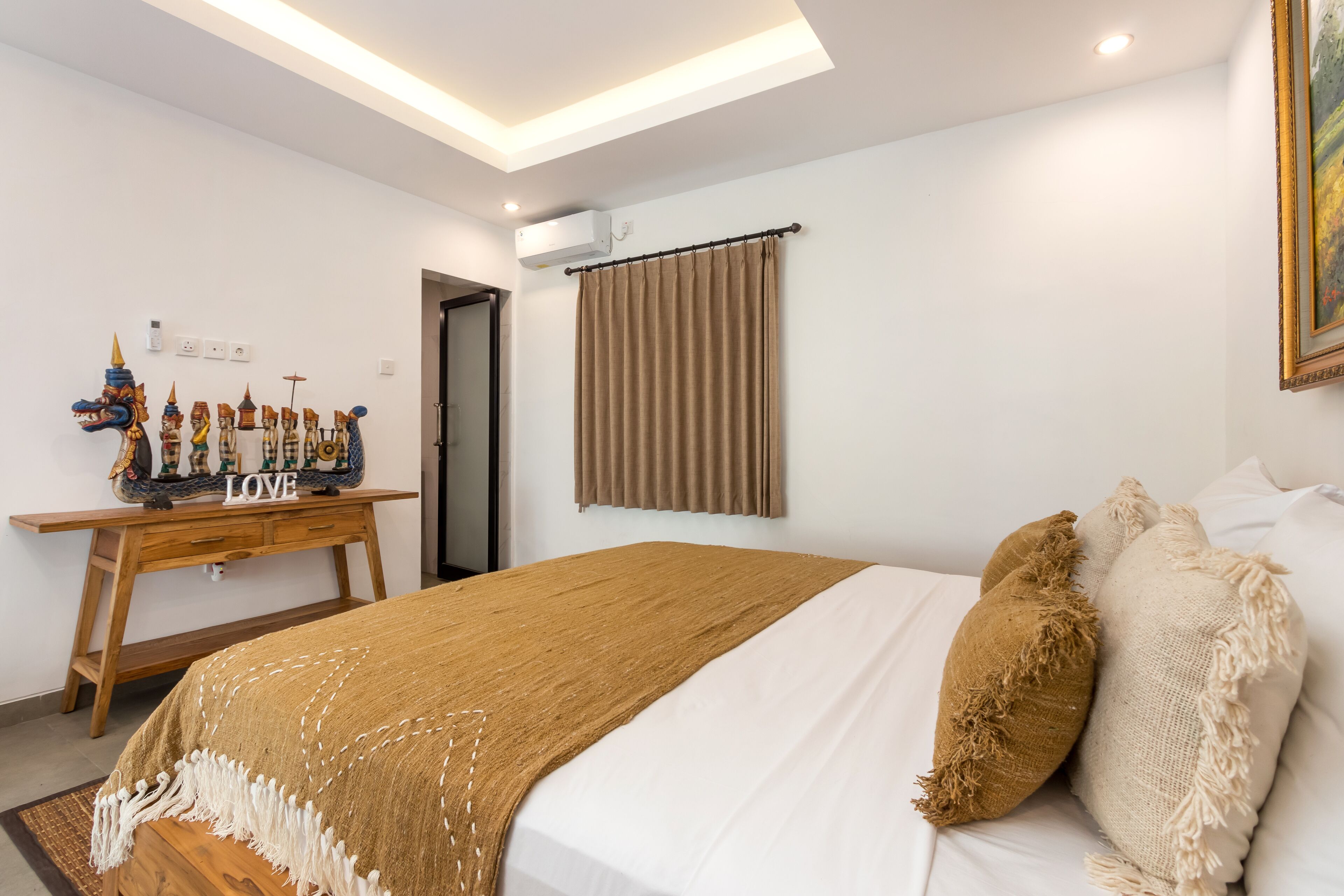 Ein Schlafzimmer mit einem Bett, einem Schreibtisch, der mit Dekorationsgegenständen bestückt ist, einem Gemälde und einem Fenster mit Vorhängen.