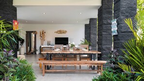 A dining area with a wooden table set for four, surrounded by stone walls and potted plants. - Villa Ambalika by Villa Finder (Seminyak)
