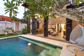 A pool area with lounge chairs, a hanging chair, and a stone pillar structure. - Villa Ambalika by Villa Finder (Seminyak)