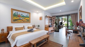 A bedroom with a large bed, bedside tables, a bench, a desk, and a bookshelf. There is a painting on the wall and a view of the outdoors through a glass door. - Villa Ambalika by Villa Finder (Seminyak)