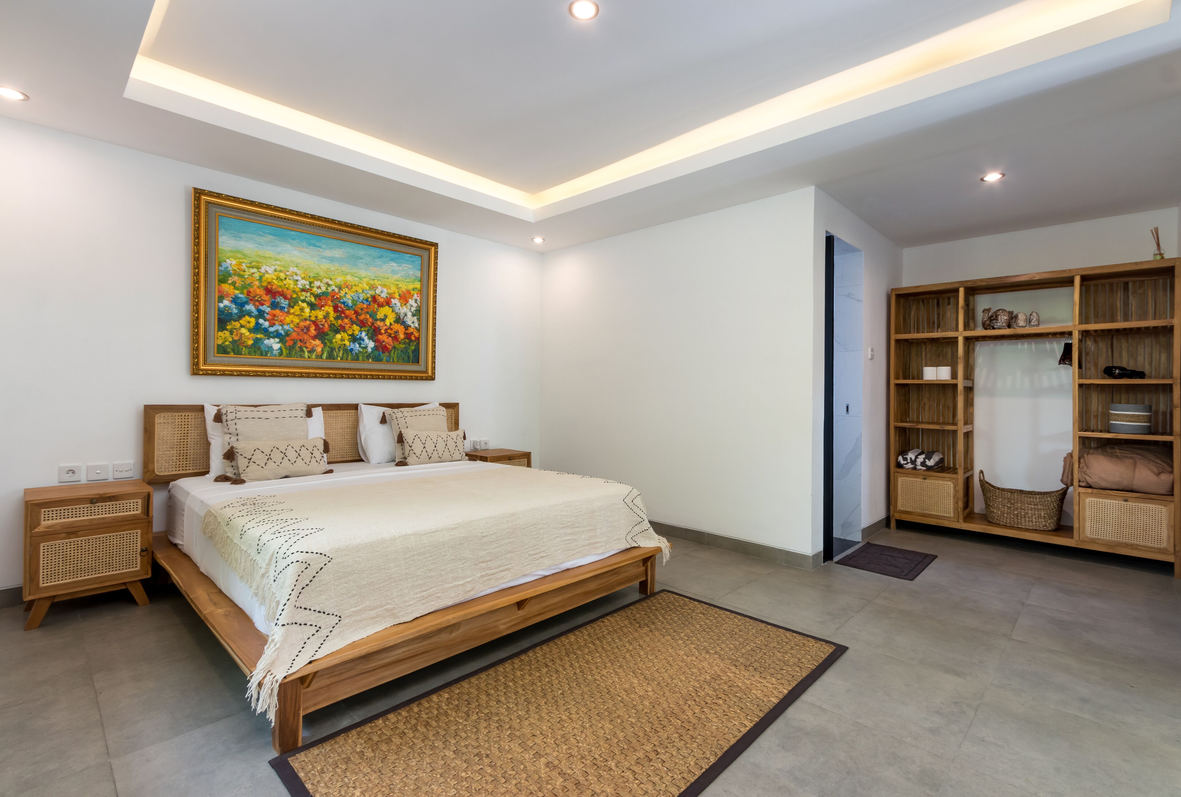 Une chambre à coucher avec un grand lit, une tête de lit en bois, des tables de chevet, un tableau, une armoire et un petit tapis.