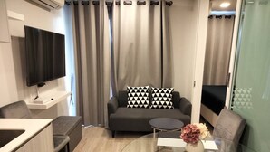 A modern living room with a sofa, a glass coffee table, and a flat-screen TV mounted on the wall.