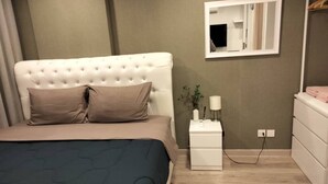A bedroom with a tufted headboard, a bed with a dark blue bedspread, a nightstand with a lamp, a mirror, and a dresser.