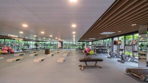 A spacious gym with various exercise equipment, large windows, and a modern design.