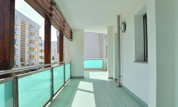 A corridor with a tiled floor, a glass railing, and a view of adjacent buildings.