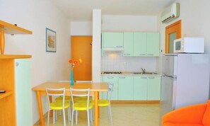 A compact kitchen with a dining table and chairs, a refrigerator, and a microwave. - Cozy Apartment by the Beach (San Michele al Tagliamento)