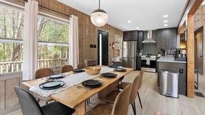 Een moderne keuken met een centraal eiland, een eethoek met een lange tafel voor vier personen, en grote ramen voorzien van gordijnen.