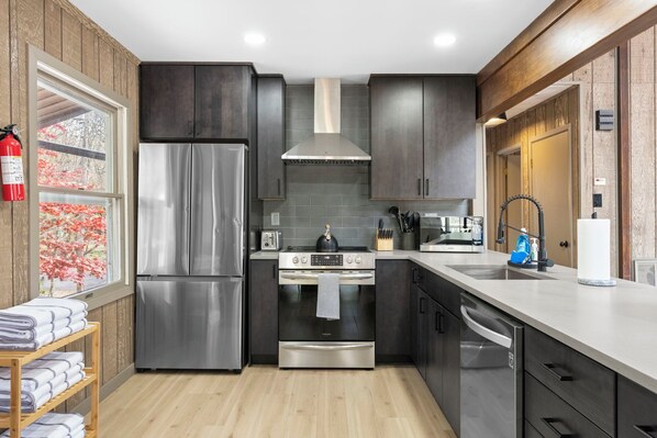 A modern kitchen with stainless steel appliances, dark cabinetry, and a wooden floor.