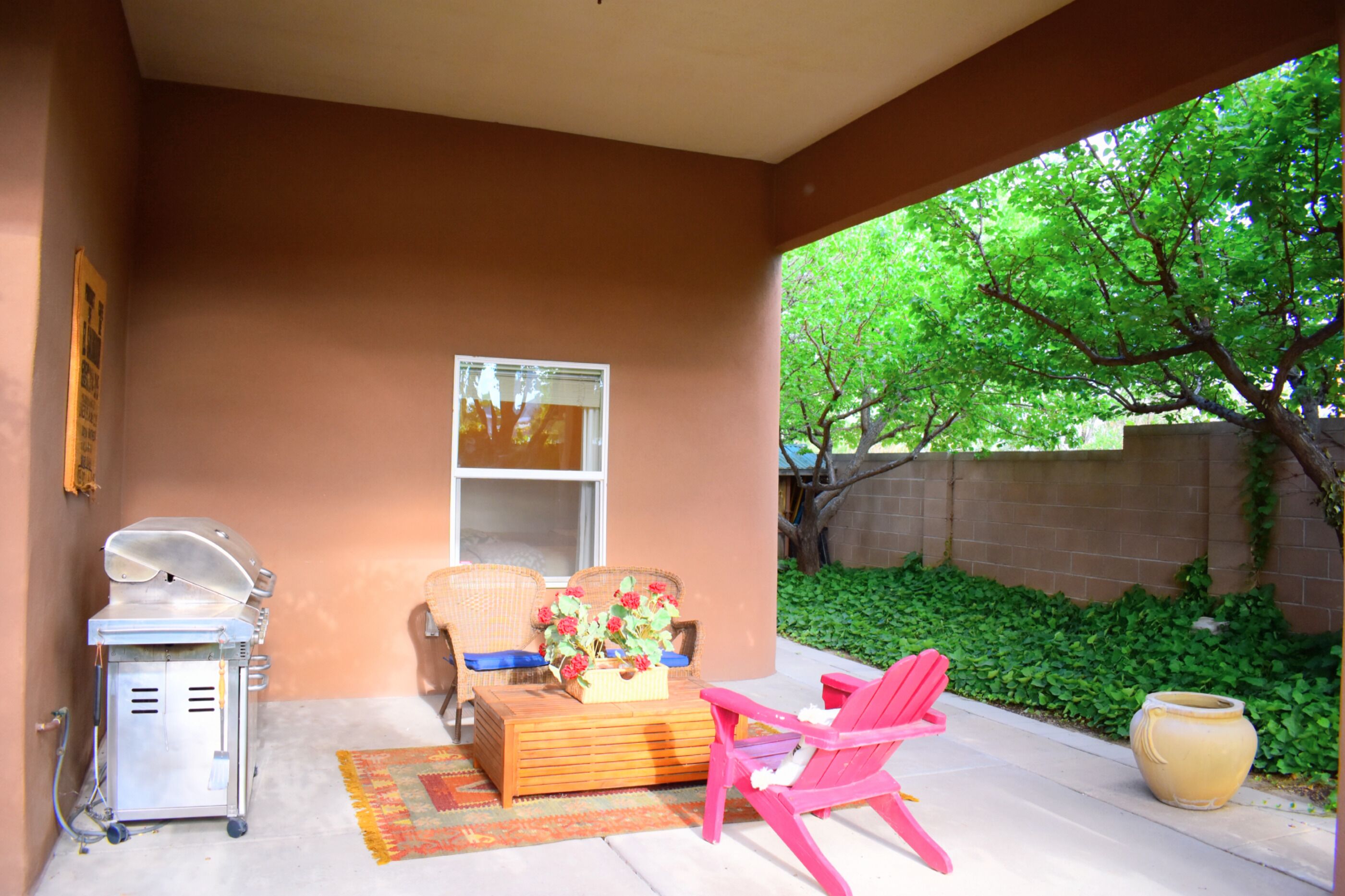 Un patio techado con una parrilla, mobiliario de mimbre y una silla rosa.