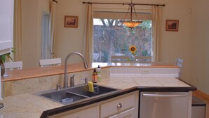 A kitchen with a sink, cabinets, a countertop, a dishwasher, and a window with a view of trees. - Rio Oasis with Southwest charm (Albuquerque)
