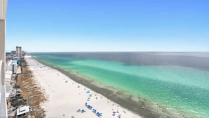 En strand med kristallklart turkosfärgat vatten, en sandstrand och en rad byggnader längs kusten.