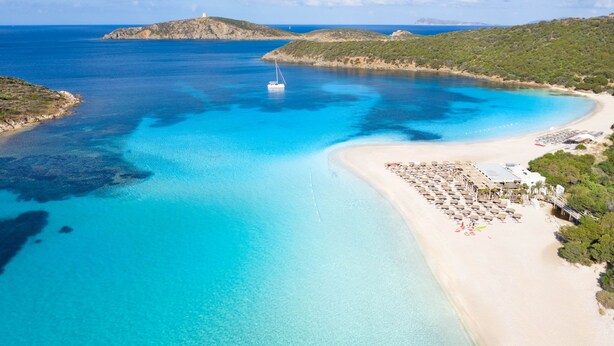 A coastal beach with a boat, clear blue waters, and a resort area with umbrellas and lounge chairs. - Simple Gem of Le Dimore di Budoni 2 Bedroom sleeps 6 (Budoni)