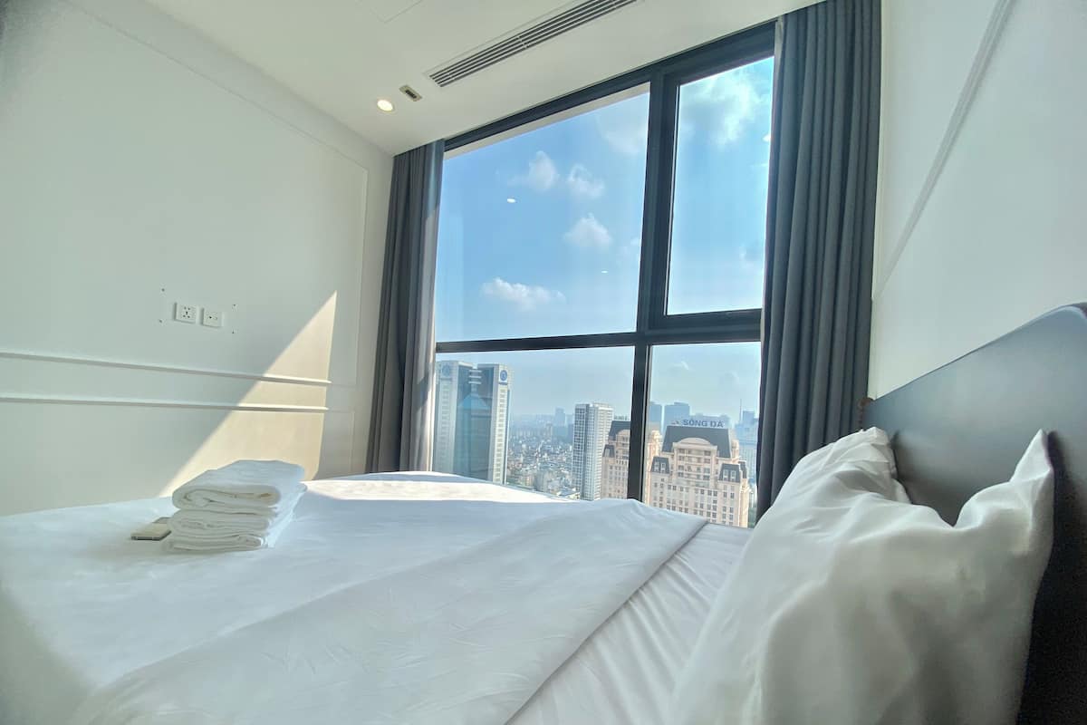 Ein Hotelzimmer mit großem Fenster, einem ordentlich bezogenen Bett und Blick auf die Stadt.