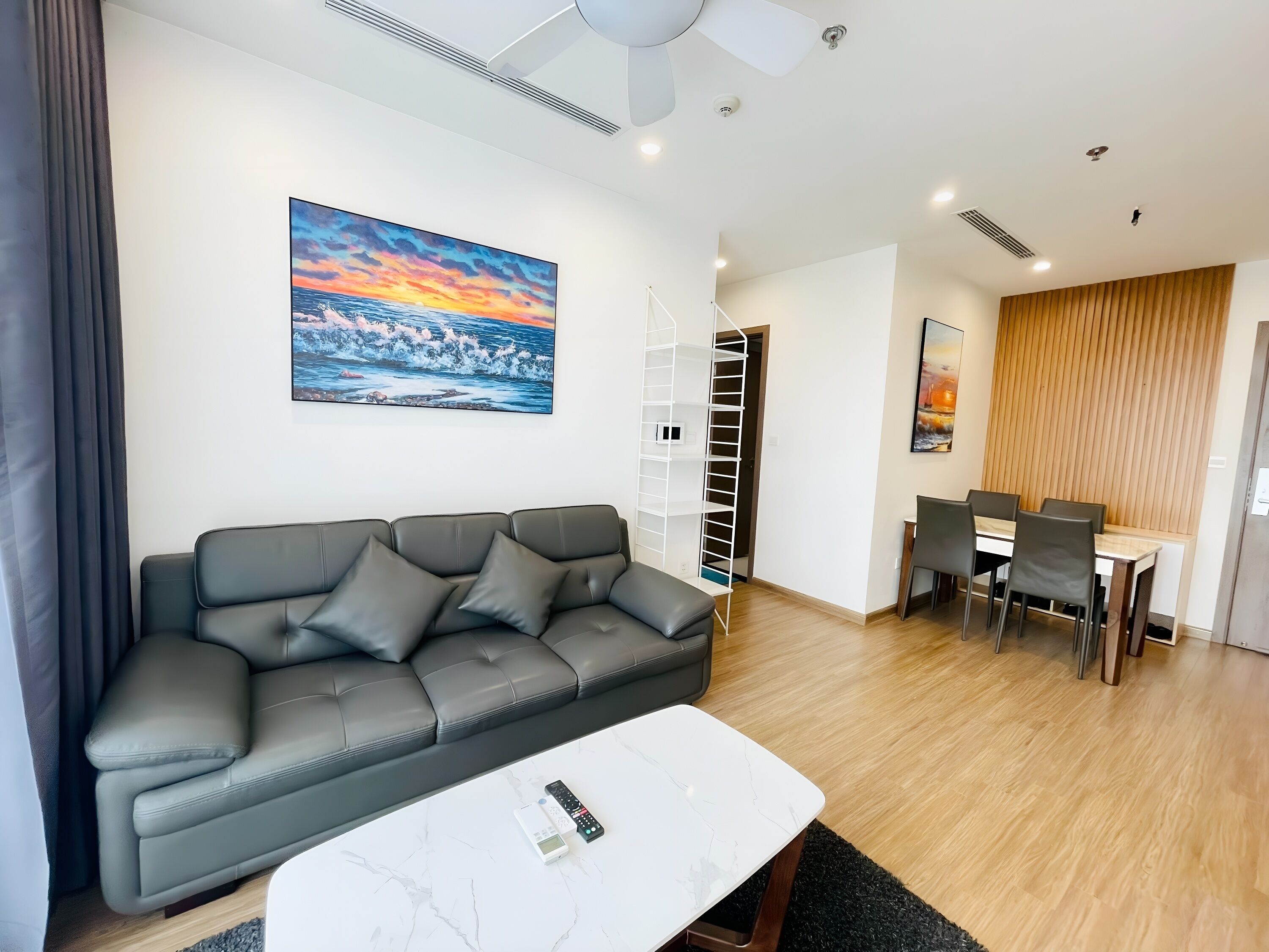A modern living room with a grey sofa, a white coffee table, and a painting of a sunset.