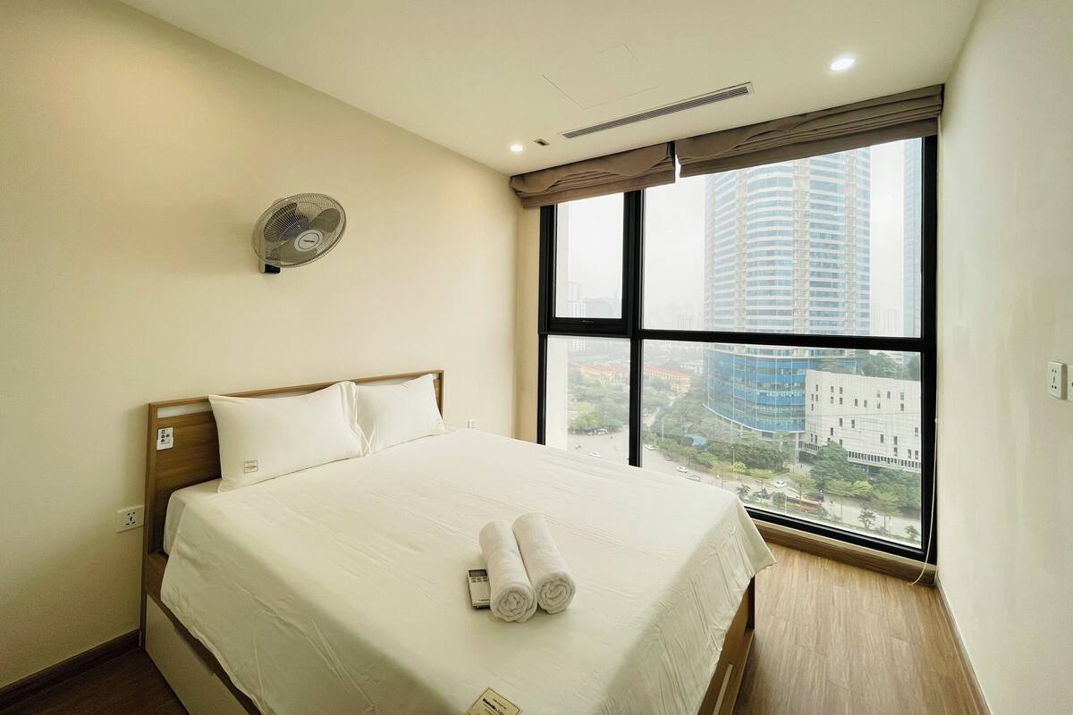 Ein Hotelzimmer mit einem großen Bett, einem Wandventilator und einem Fenster mit Blick auf die Stadt.