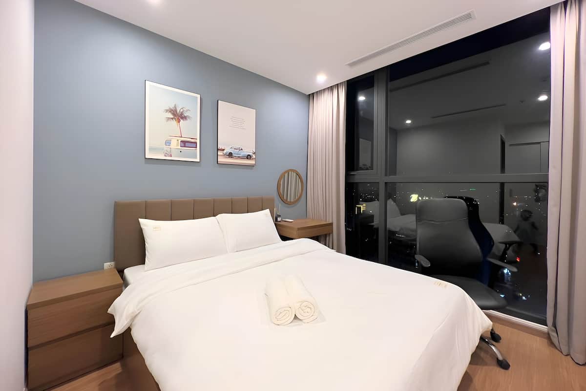 Ein modernes Hotelzimmer mit einem großen Bett, einem Nachttisch, einem Schreibtisch und einem großen Fenster mit Blick auf die Stadt.