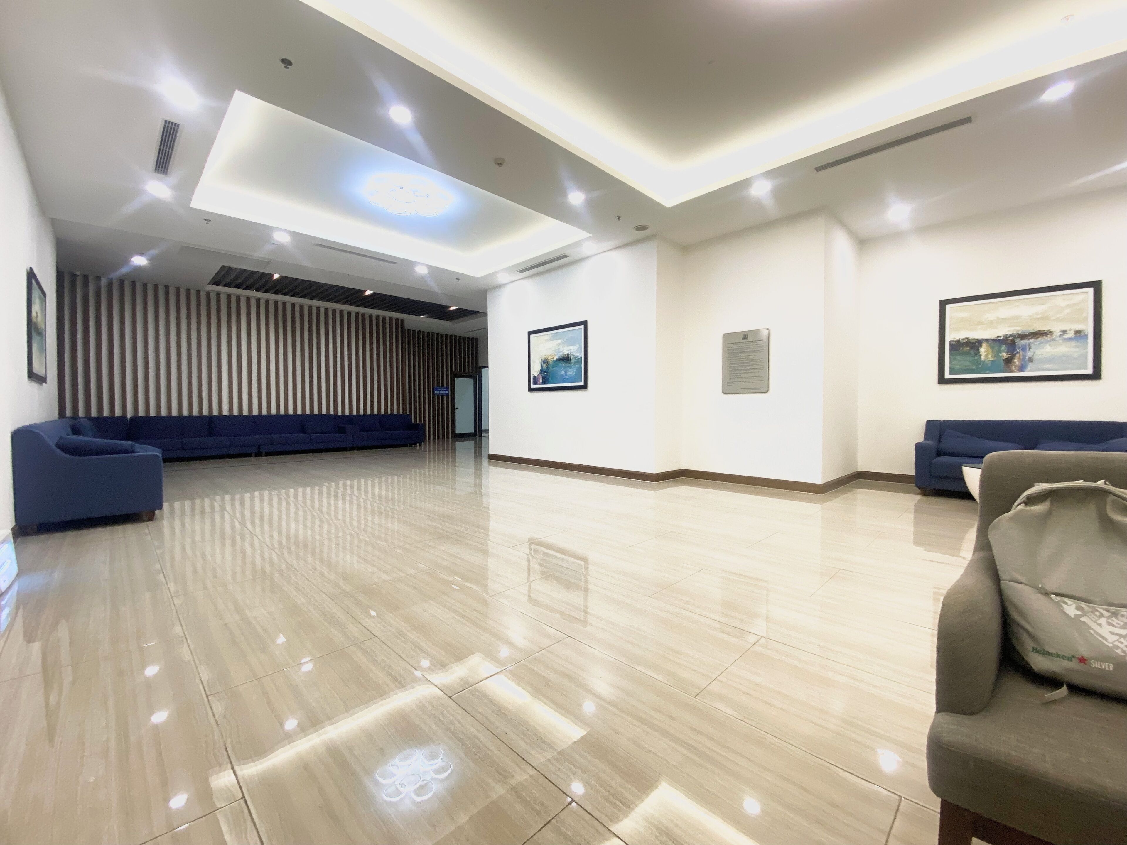 A spacious lobby with a polished floor, a blue sofa, and a Heineken-branded chair.