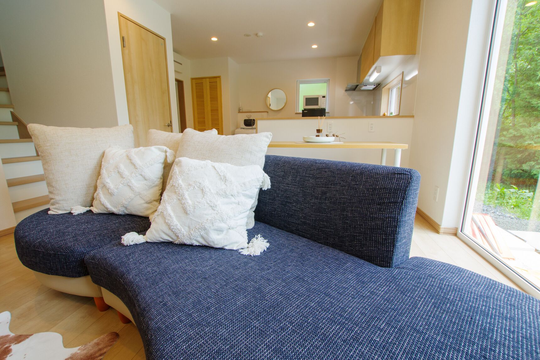A modern living room with a blue sofa, white cushions, and a wooden staircase.