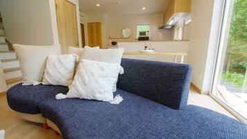 A modern living room with a blue sofa, white cushions, and a wooden staircase.