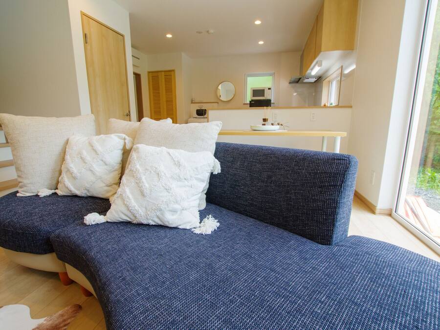 A modern living room with a blue sofa, white cushions, and a wooden staircase.