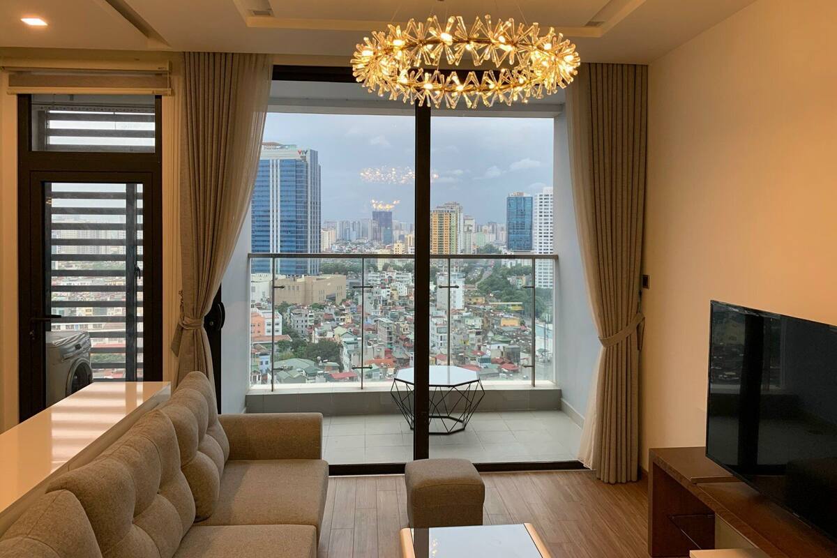 A modern living room with a large window, a sofa, a TV, and a chandelier.