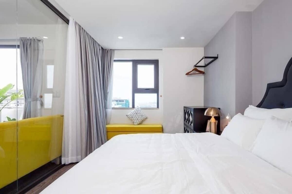 A modern bedroom with a large bed, a bedside table, a lamp, and a window with curtains.