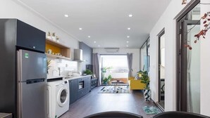 Een moderne keuken met een wasmachine, een eethoek met een gele stoel en uitzicht op het buitengebied.