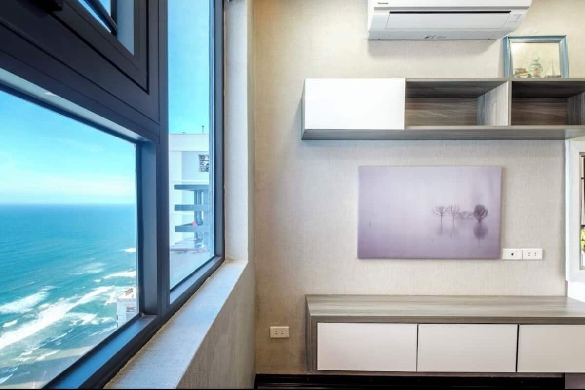A modern room with a large window overlooking the ocean, built-in shelving, and a framed artwork on the wall.