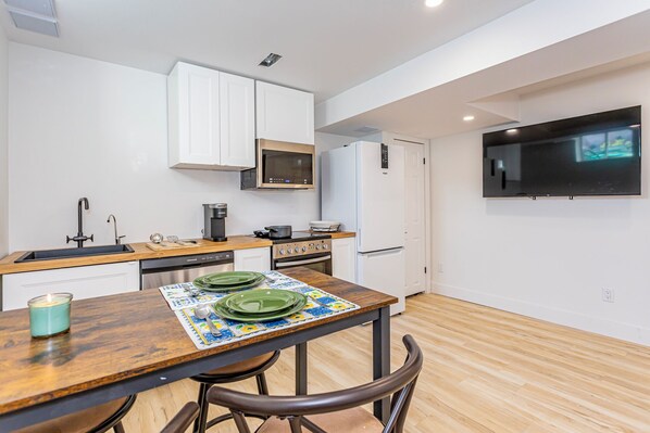 A modern kitchen with white cabinets, a microwave, stove, and a refrigerator. There is a dining table with chairs and a candle on it.