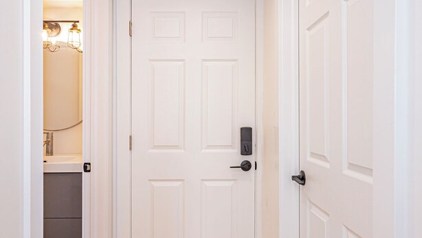 A hallway with a wooden floor, white walls, and a white door with a keyhole lock. - Newly renovated cozy studio (Woodstock)