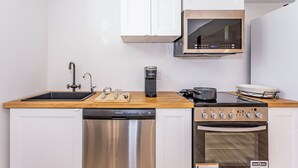 A compact kitchen with a dishwasher, stove, microwave, and a coffee maker. - Newly renovated cozy studio (Woodstock)