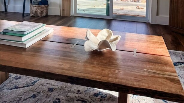 A room with a wooden table, books, a decorative object, a bench, and a view through large windows.