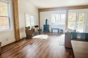 Een ruime woonkamer met houten vloeren, een groot raam, een open haard en een bank.