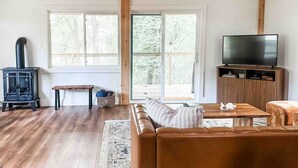 A living room with a sofa, a television, a wooden floor, a fireplace, and large windows.