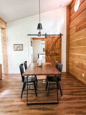 Ein Essbereich mit Holztisch, schwarzen Stühlen, einer Pendelleuchte und einer Holztür.