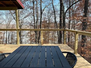 Eine Holzterrasse mit Tisch und Stühlen, umgeben von Bäumen und einem klaren Himmel.