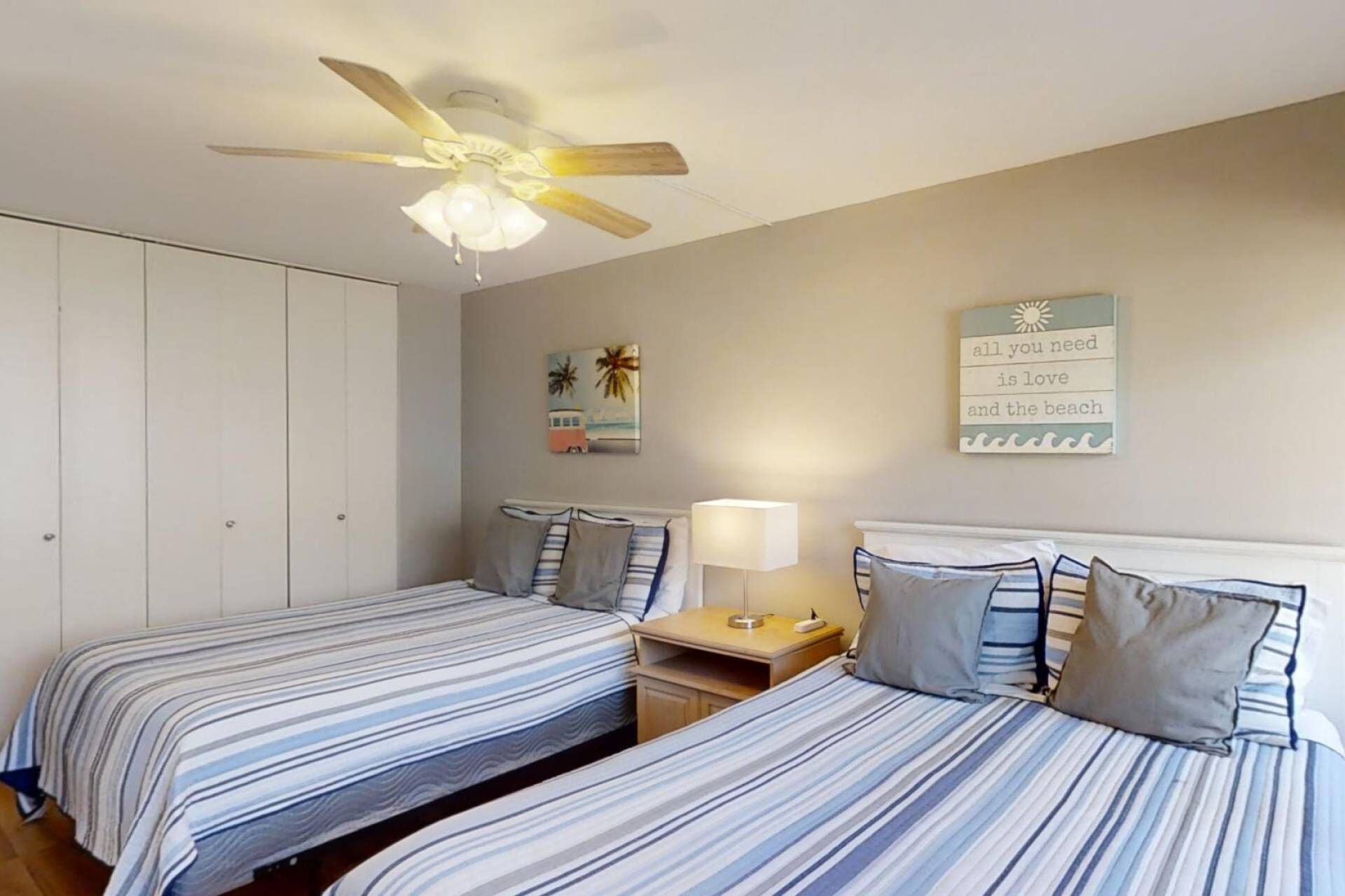 A bedroom with two beds, a ceiling fan, a nightstand with a lamp, and a wall with a motivational quote.
