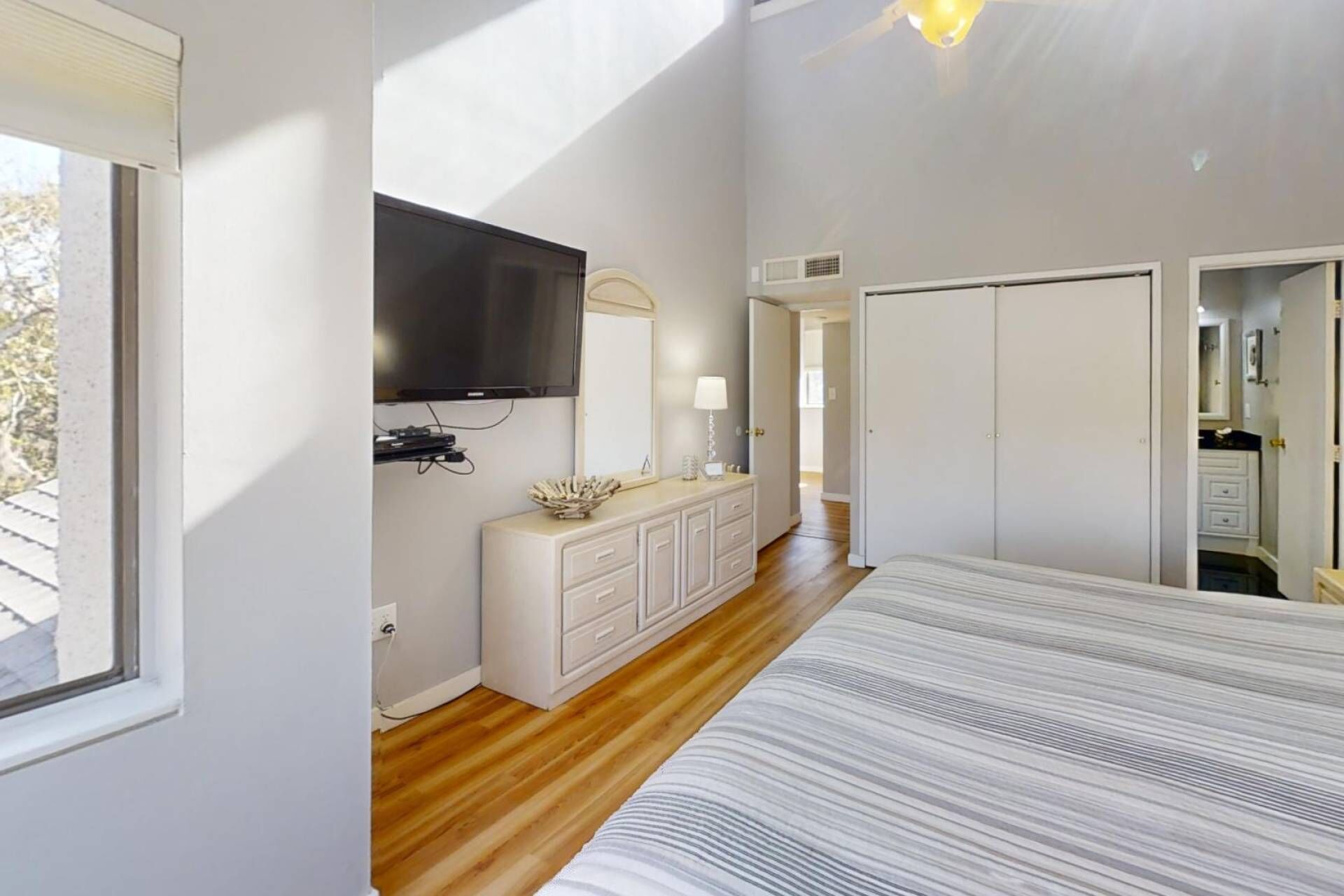 Un dormitorio con cama, televisor montado en la pared, cómoda y vestidor.