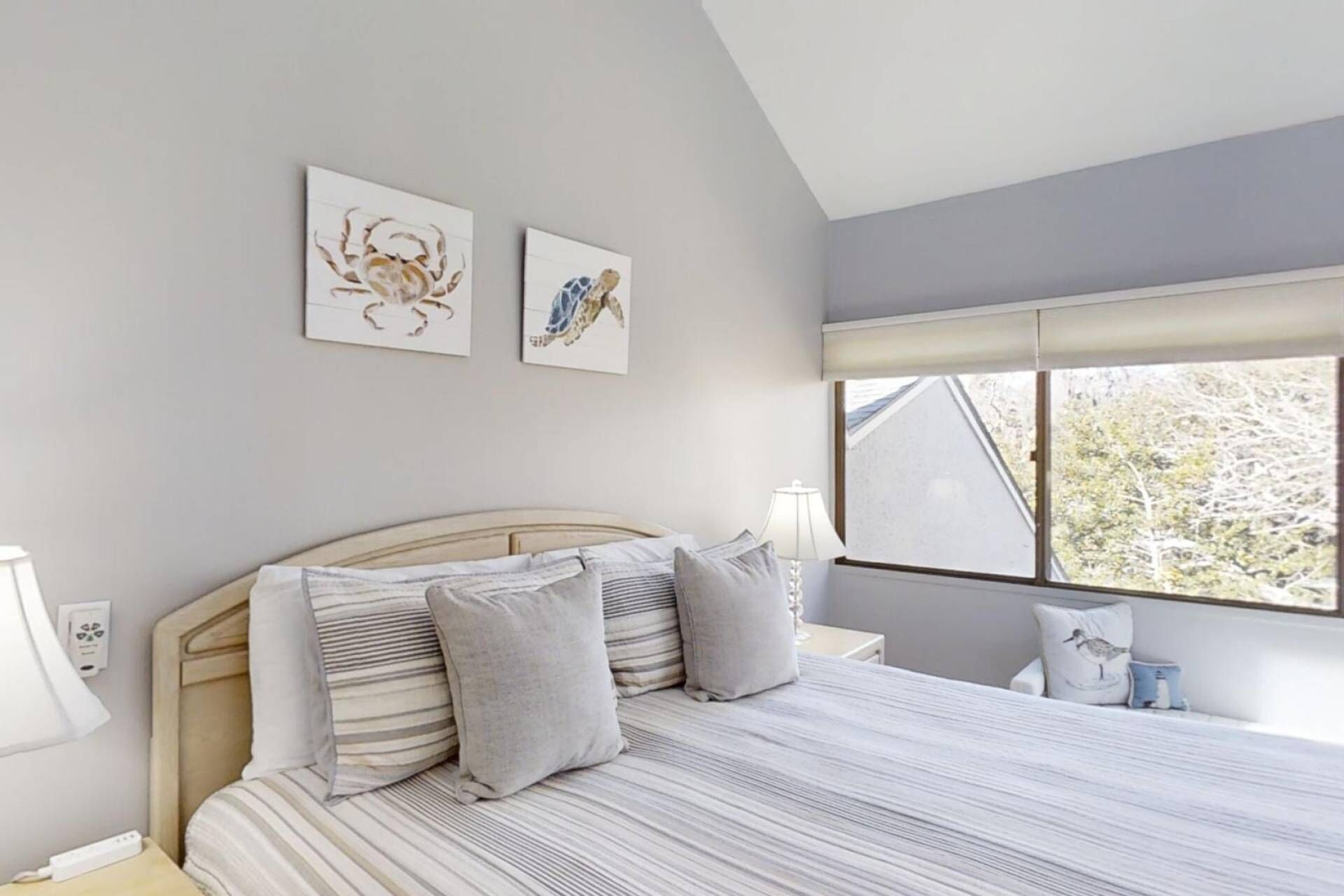 Een slaapkamer met een groot bed, een nachtkastje, een lamp en een raam met uitzicht op bomen.
