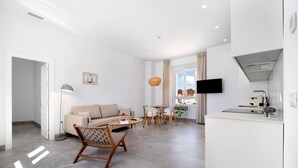 A modern living room with a sofa, coffee table, and chairs, a dining area with a table and chairs, a kitchen with a stove, and a TV mounted on the wall.