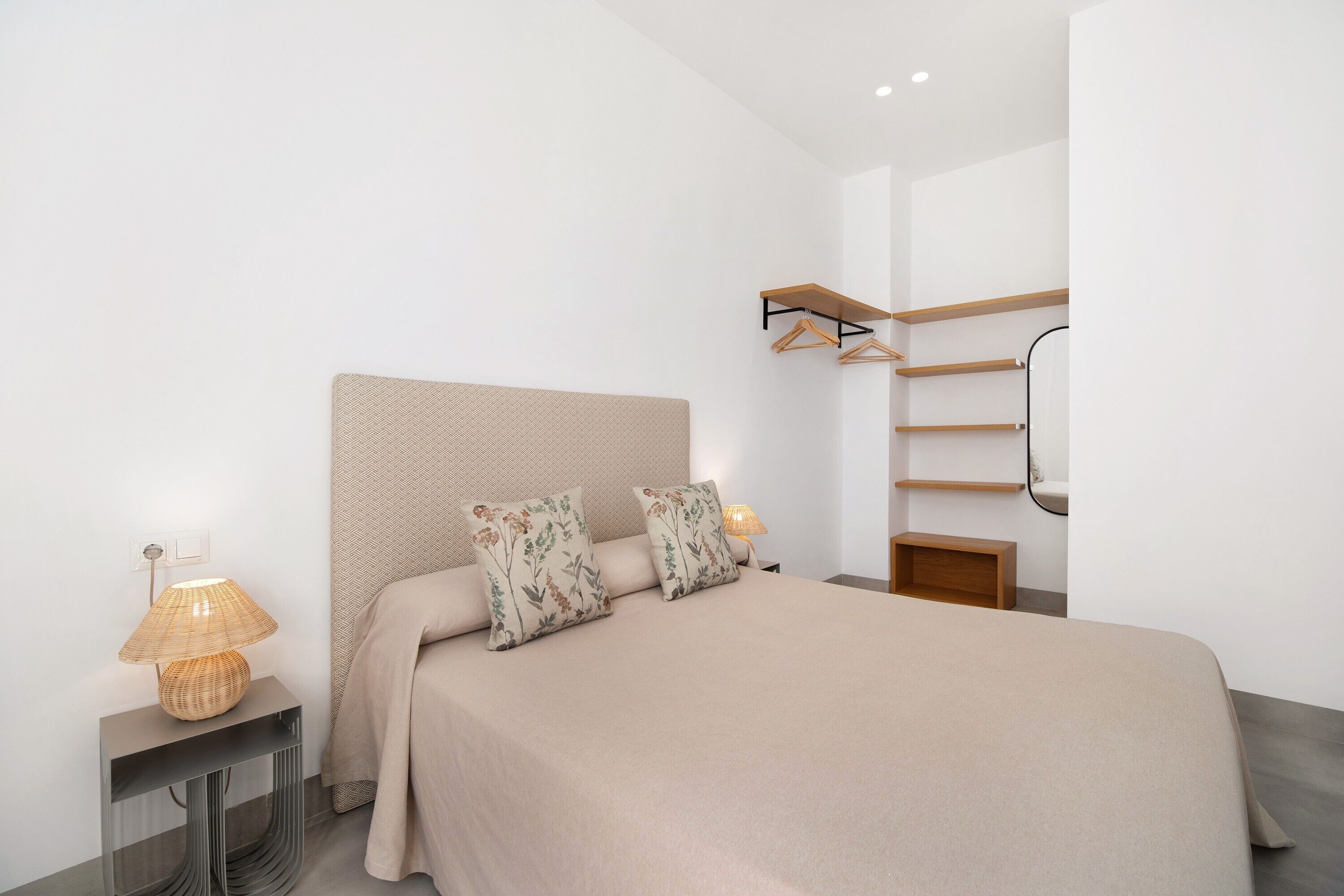 Une chambre à coucher moderne avec un lit, des lampes de chevet, une tête de lit et une étagère fixée au mur.