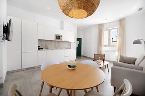 Een moderne keuken met witte kasten, een magnetron en een eethoek met een ronde houten tafel en stoelen.