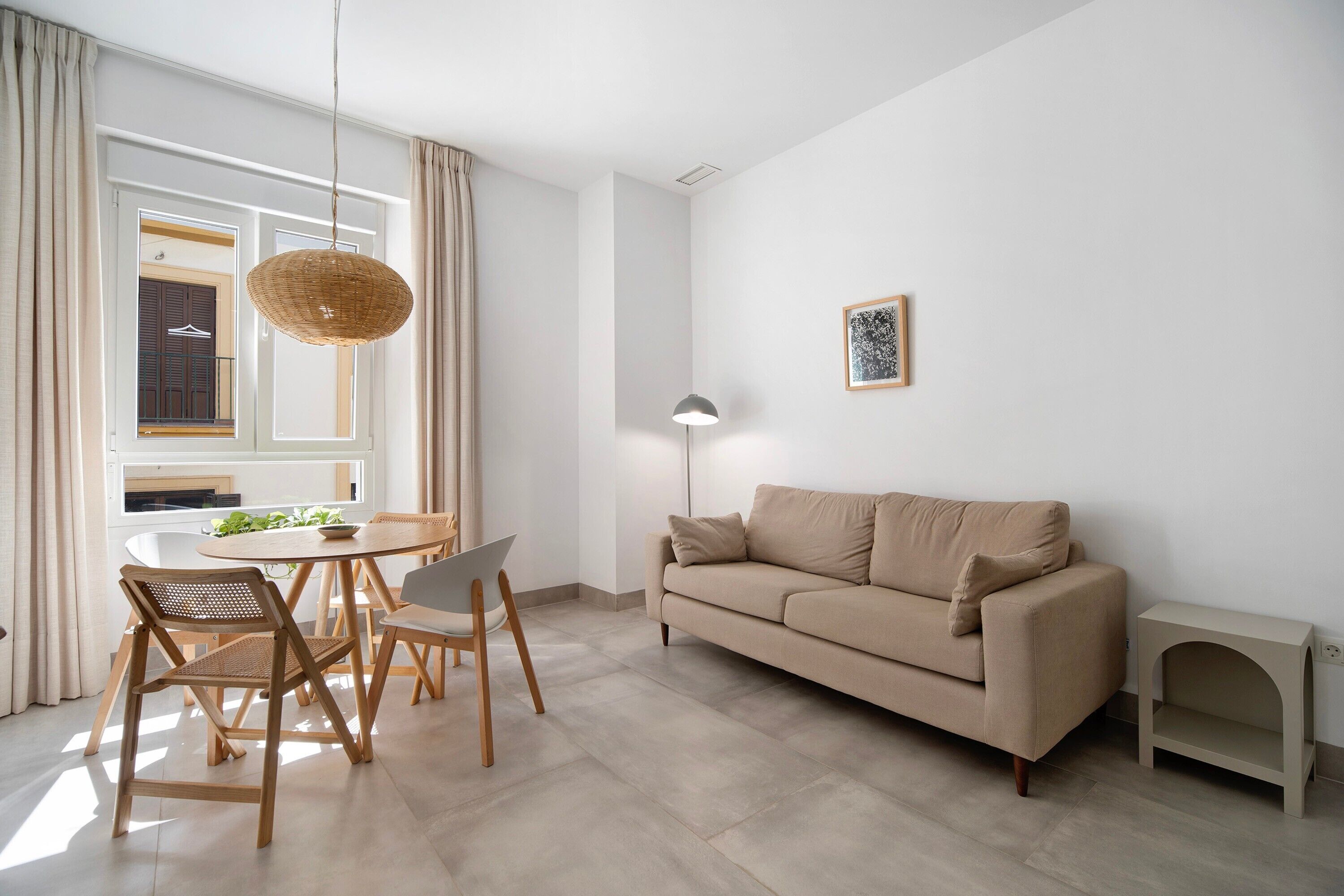 A modern living room with a sofa, dining table, chairs, and a hanging light fixture.