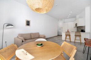 A modern kitchen with white cabinets, a dining area with a round wooden table and woven chairs, and a hanging light fixture.