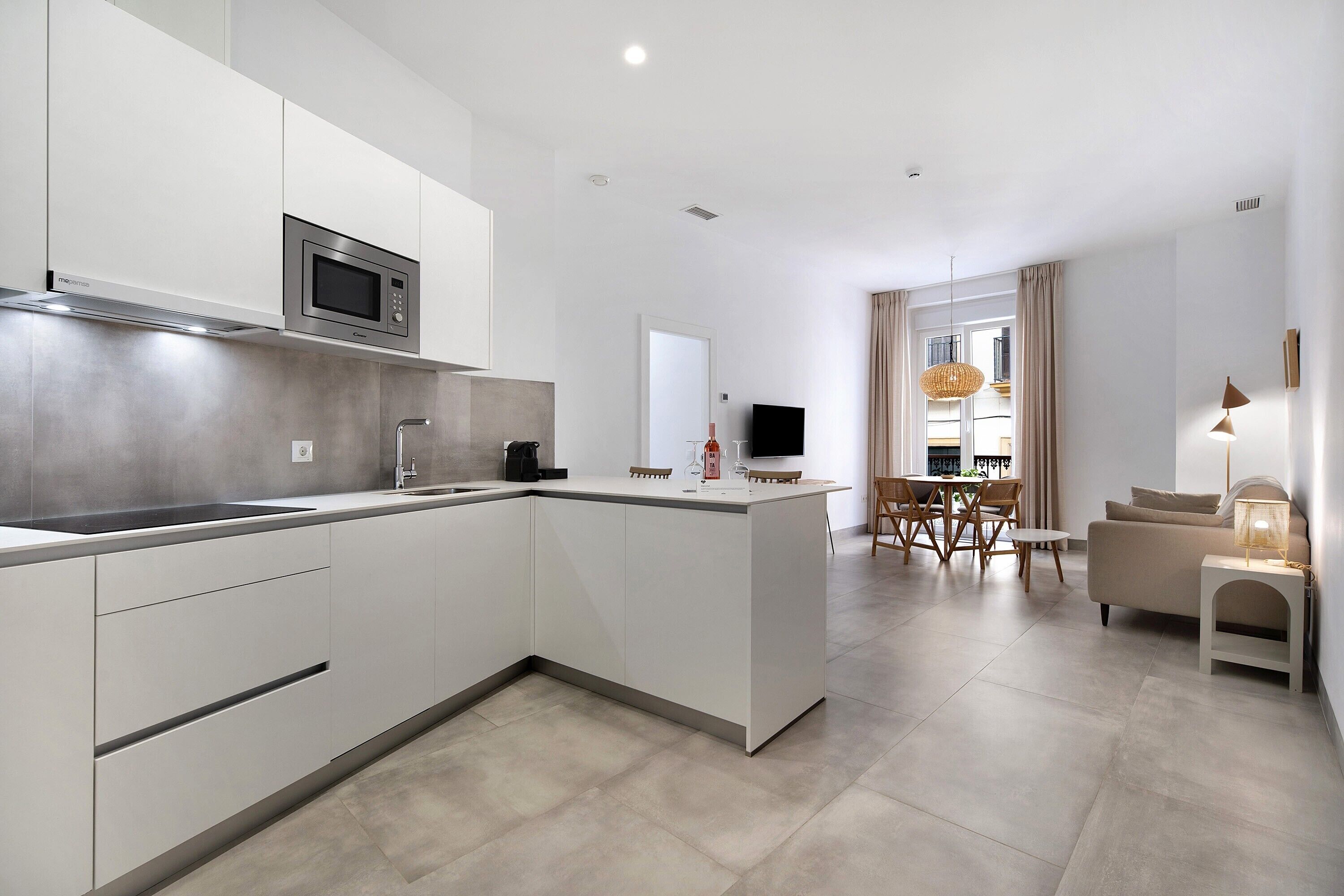 A modern kitchen with a built-in microwave, a dining area with a table and chairs, and a living space with a sofa and lamp.
