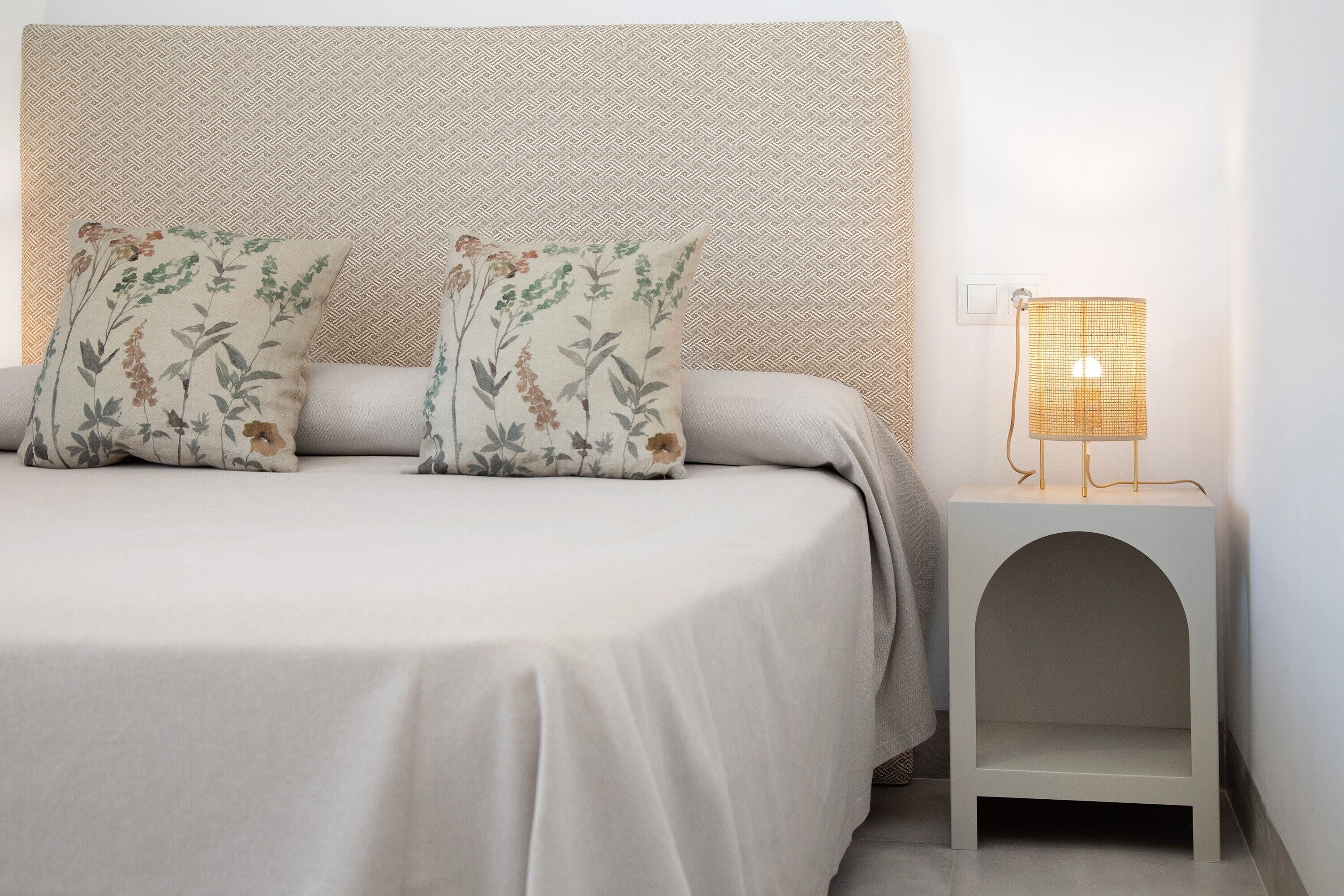 Una cama con almohadones estampados, una lámpara de noche y un cabecero sencillo.