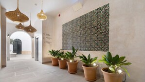 Un pasillo con plantas en macetas, lámparas de mimbre colgantes y un papel tapiz estampado.