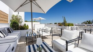 Un área de estar al aire libre con mobiliario blanco, sombrillas y una vista despejada del cielo.
