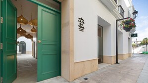 Entrada de un hotel con una puerta verde, un cartel que dice 'Casa Pela Vega Suites' y macetas colgantes con flores.